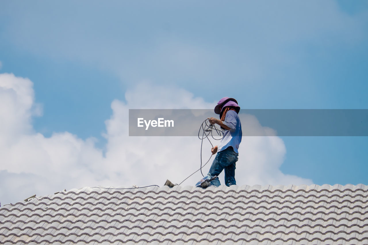 LOW ANGLE VIEW OF MAN HOLDING UMBRELLA ON ROOF