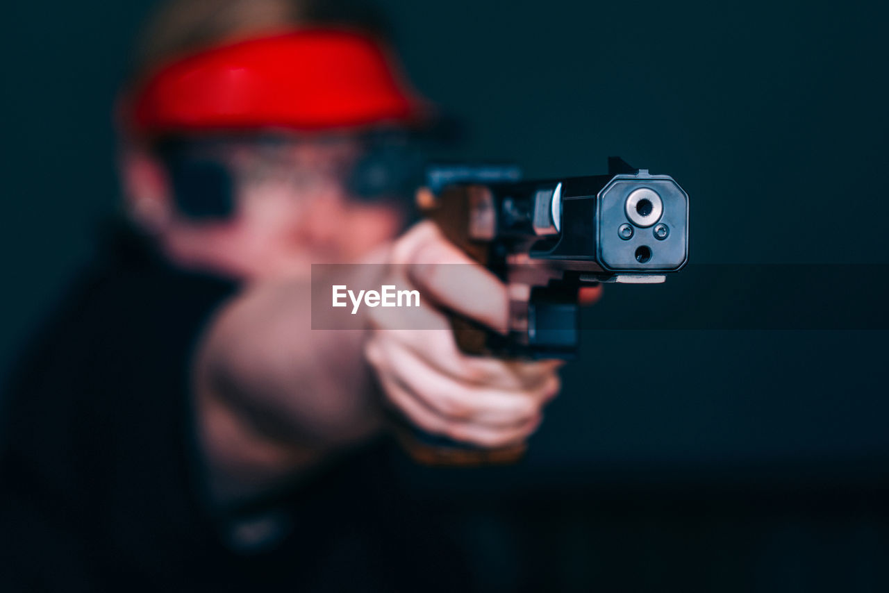 Close-up of woman aiming gun against black background