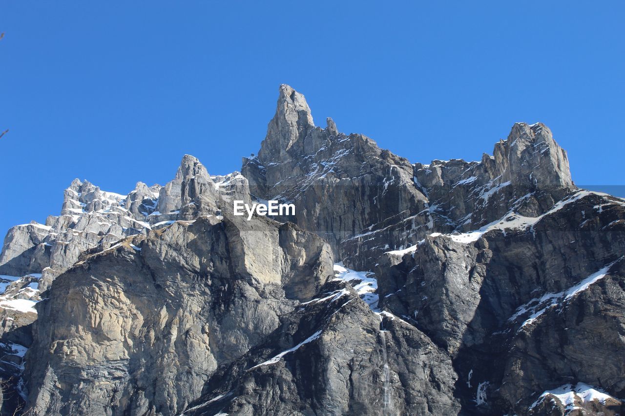 Low angle view of snowcapped mountains against clear blue sky