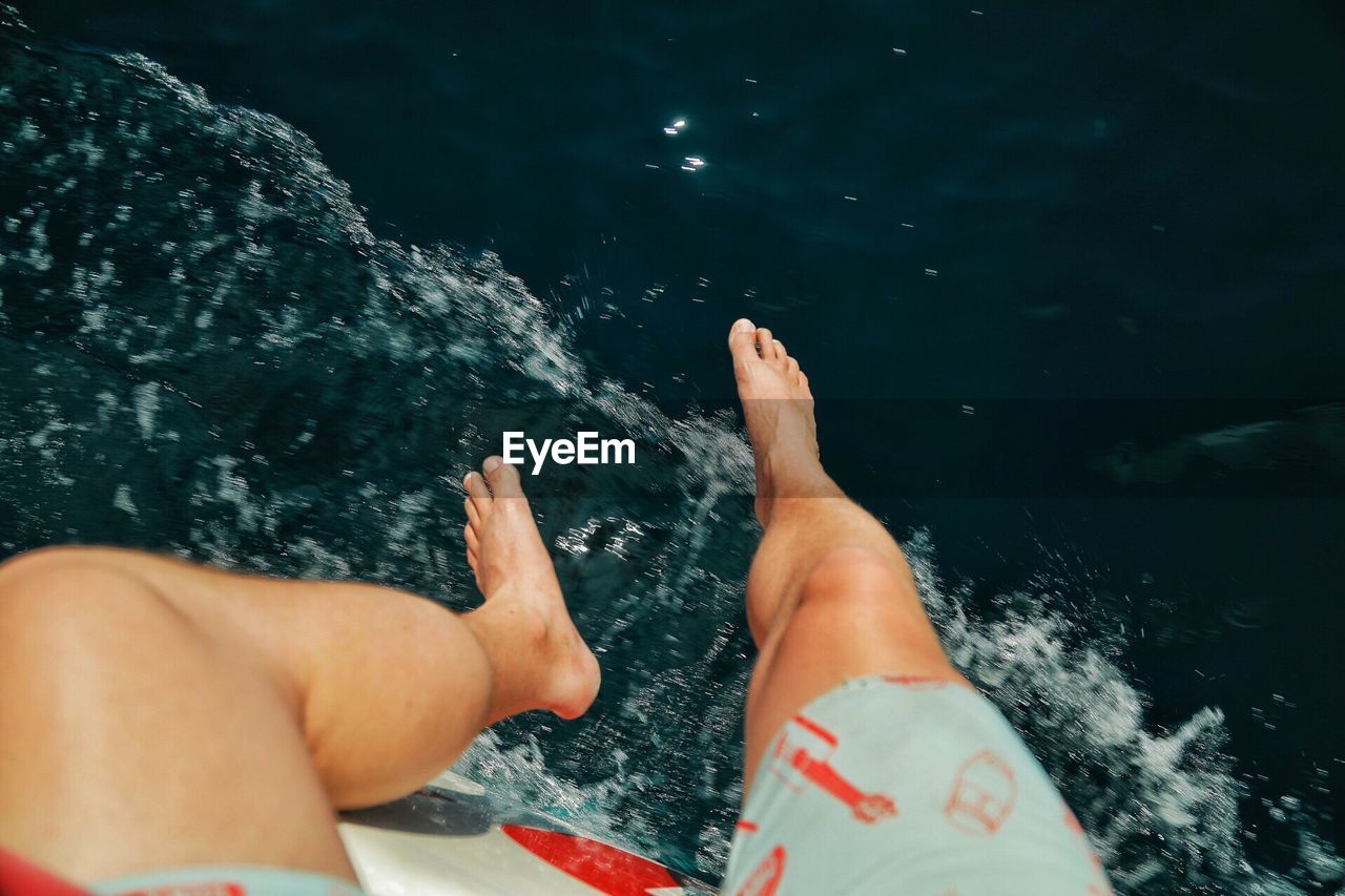 Low section of man sitting on boat at sea during sunny day