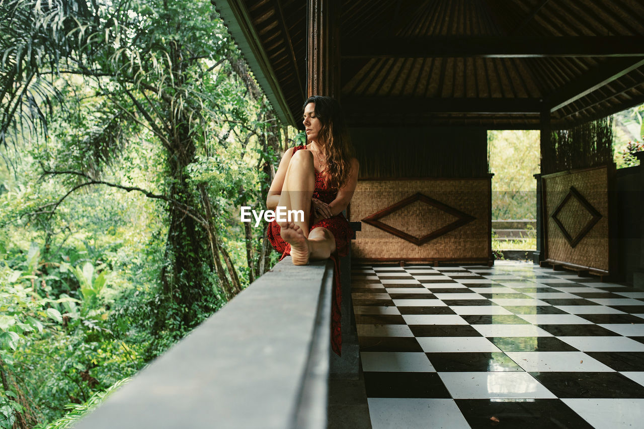 Full length of girl sitting on wall against plants