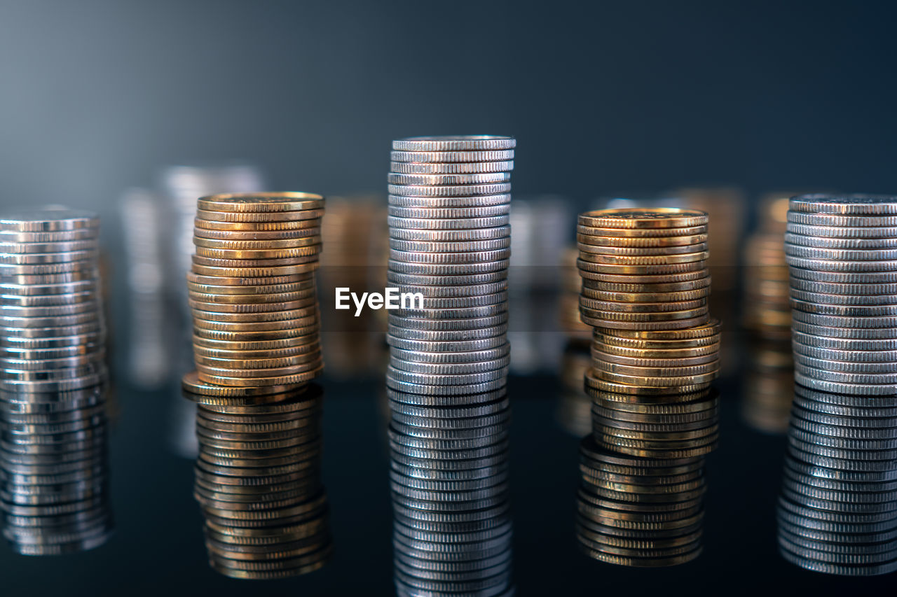 Piles of coins on a black, reflective surface seen from the top. inflation consuming our savings. 