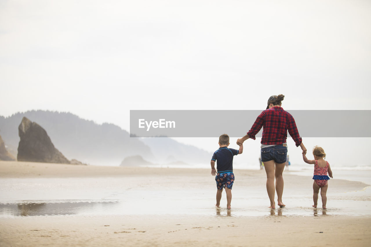 Rear view of mother walking on beach with her two young children.