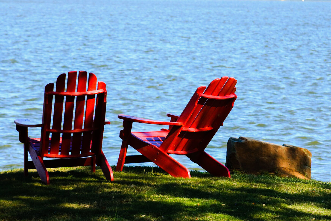 Empty lounge chairs on field by lake