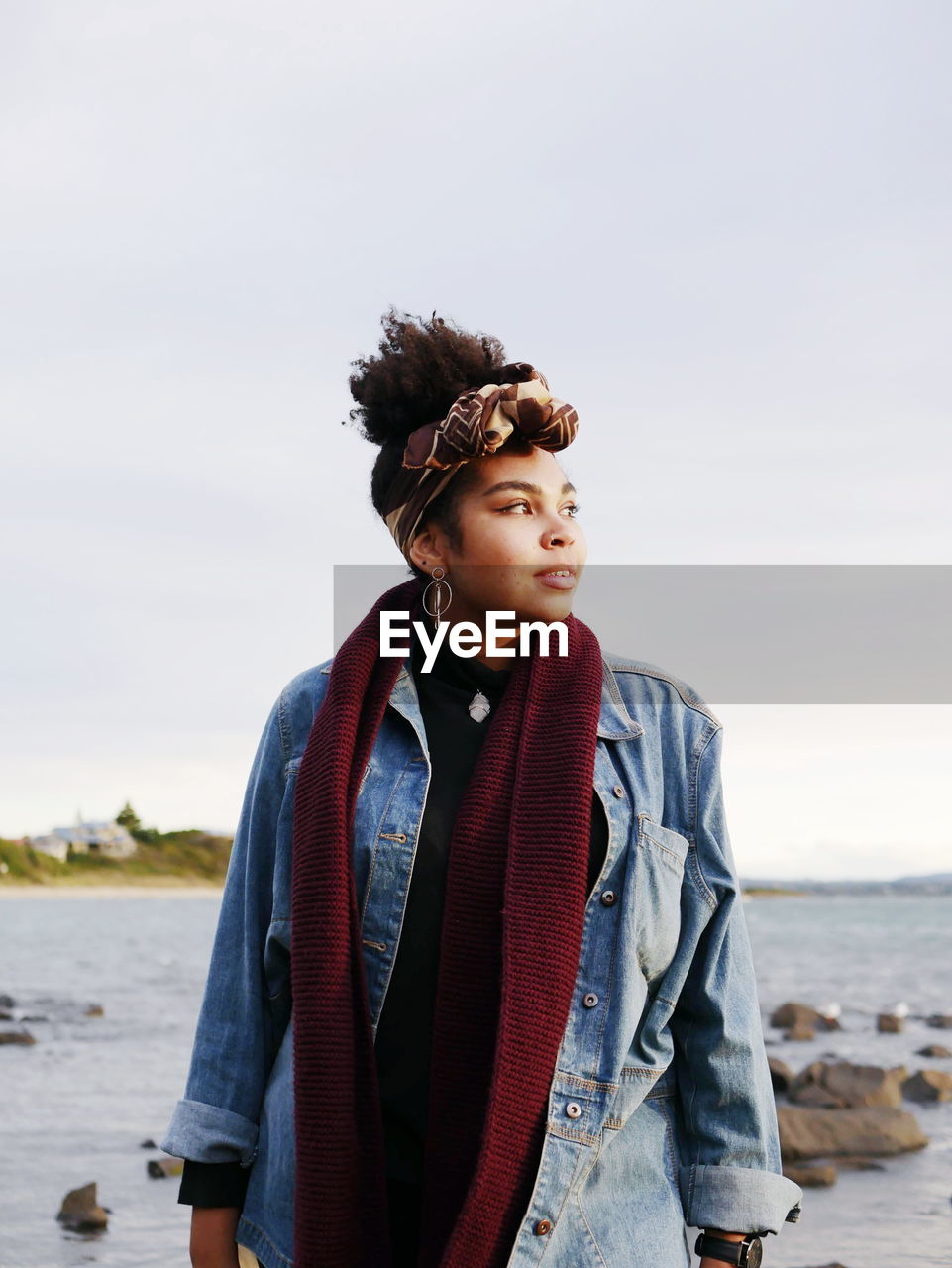 Thoughtful young woman standing at beach against sky