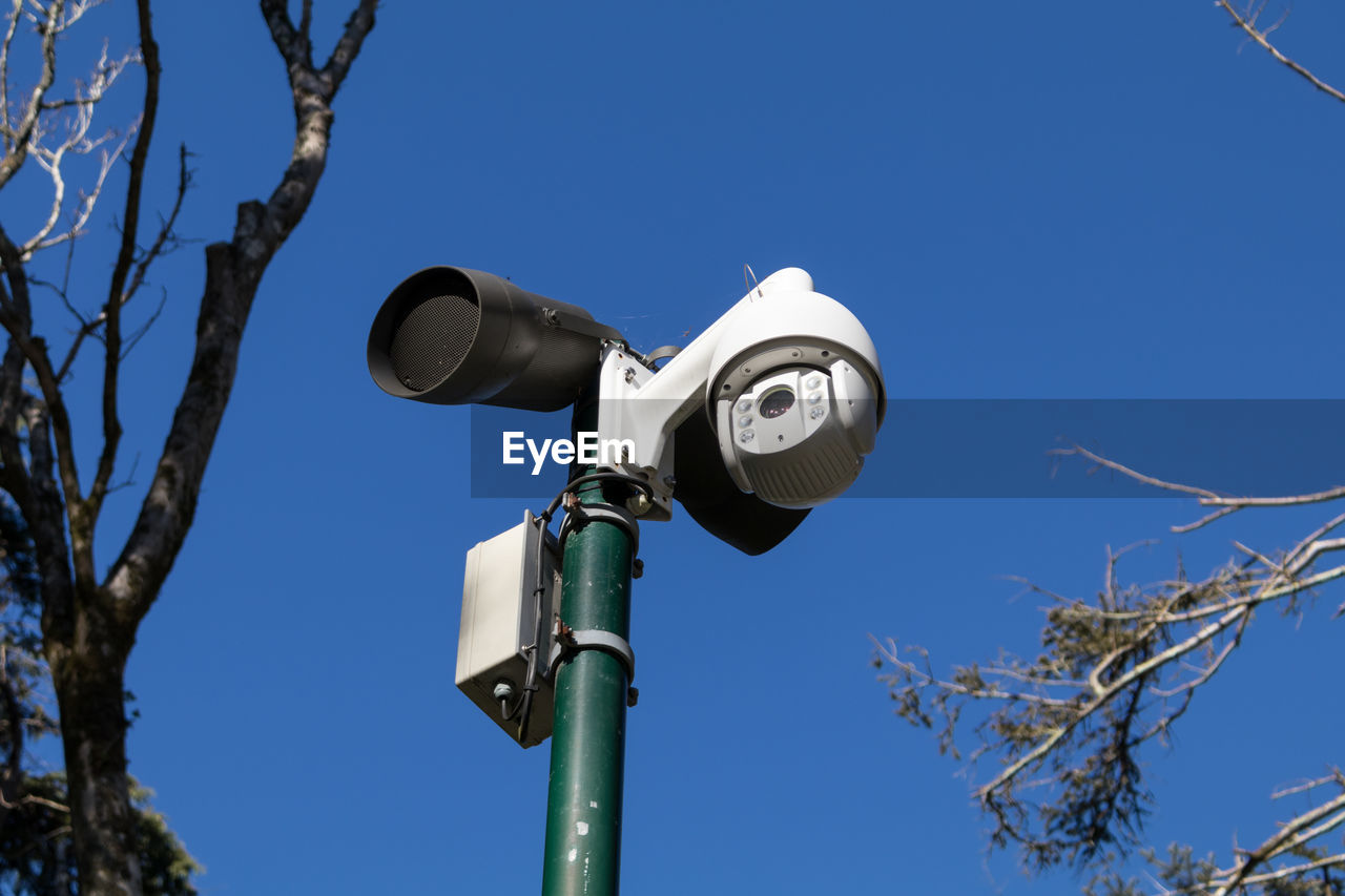 Low angle view of security camera against clear blue sky