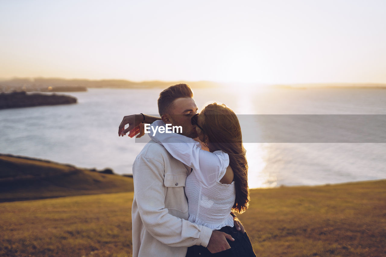 Romantic young couple kissing while standing on hill at mirador de la providencia, gijon, spain