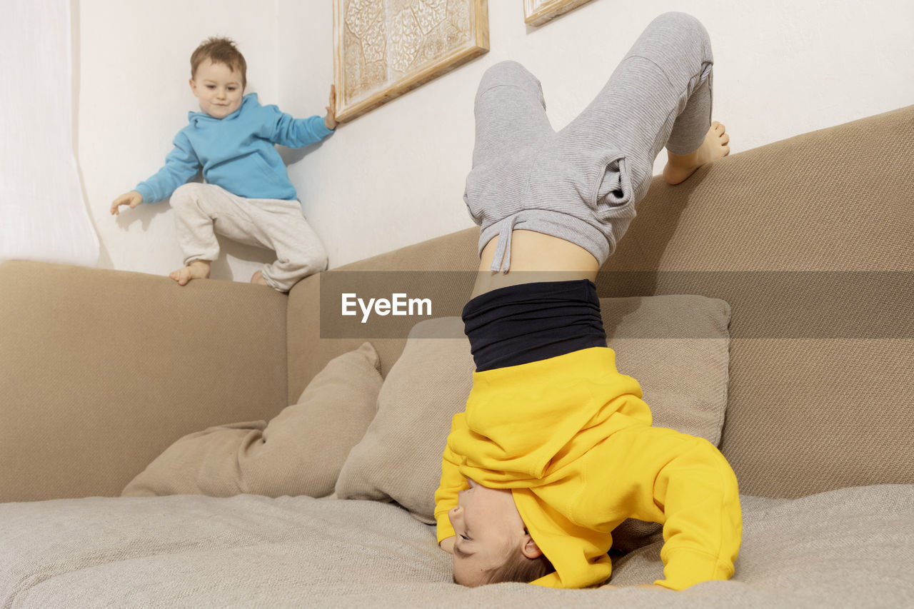 Two active, little kids doing gymnastic handstand exercise in living room. 