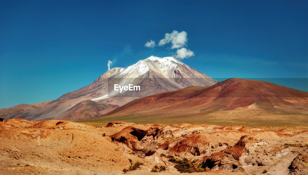 Scenic view of volcanic mountain against blue sky