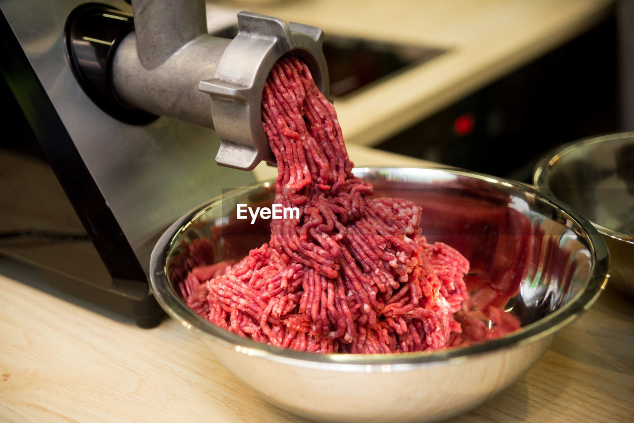 Minced meat comes out of the mincer in a metal bowl, the process of minced meat preparation