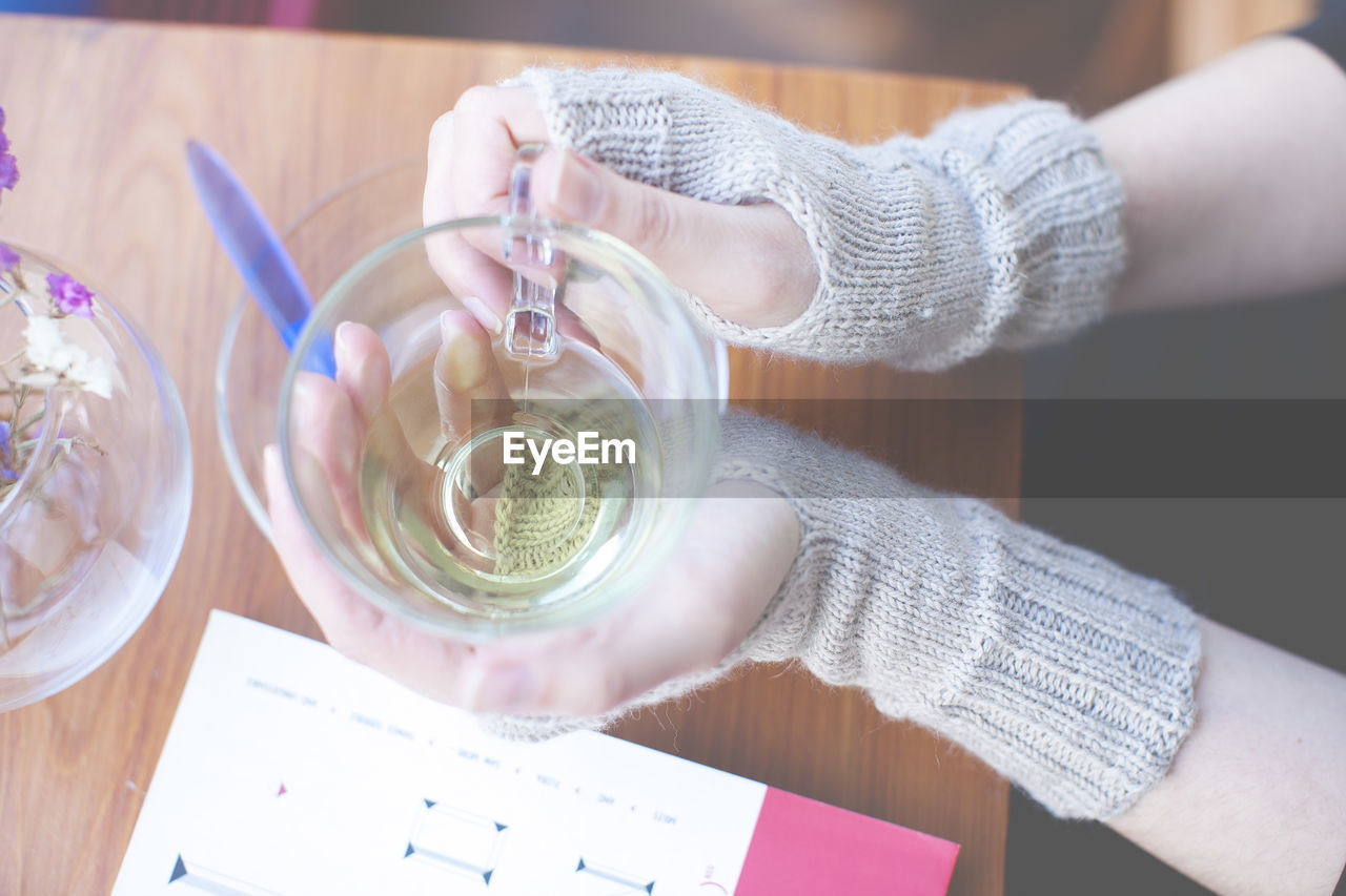 Cropped image of woman wearing mitten holding tea cup at cafe