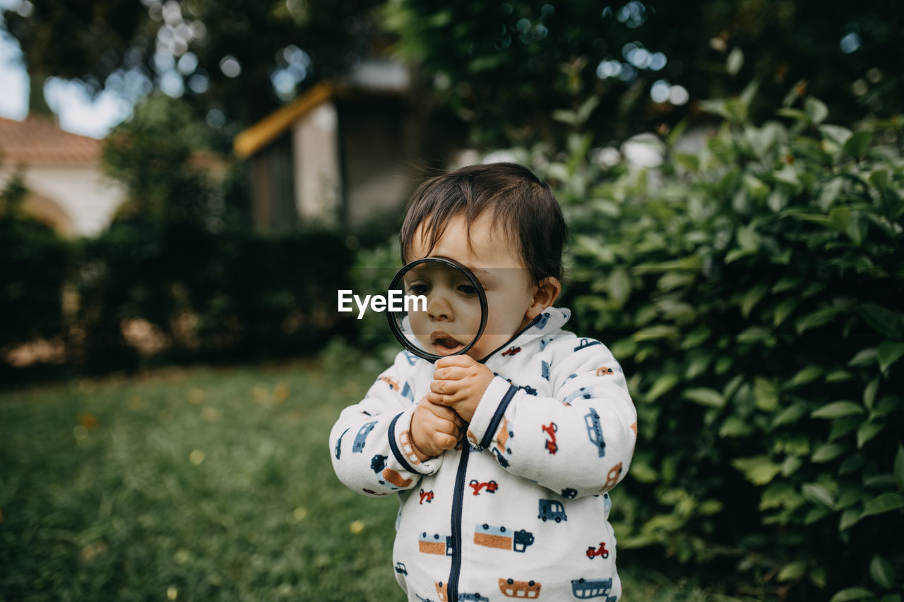 Cute boy standing playing with magnifying glass