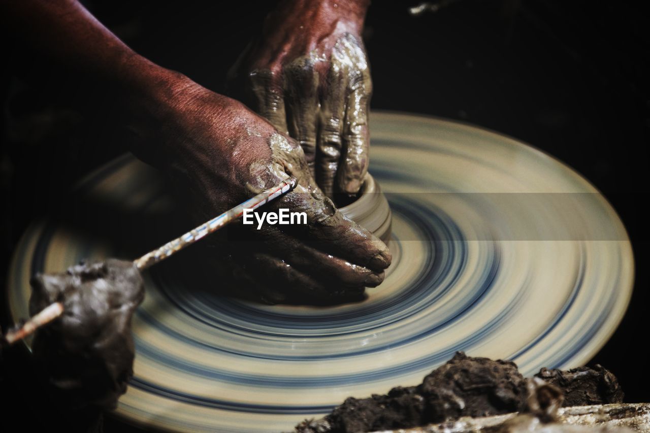 Cropped image of man shaping earthenware on pottery wheel at workshop
