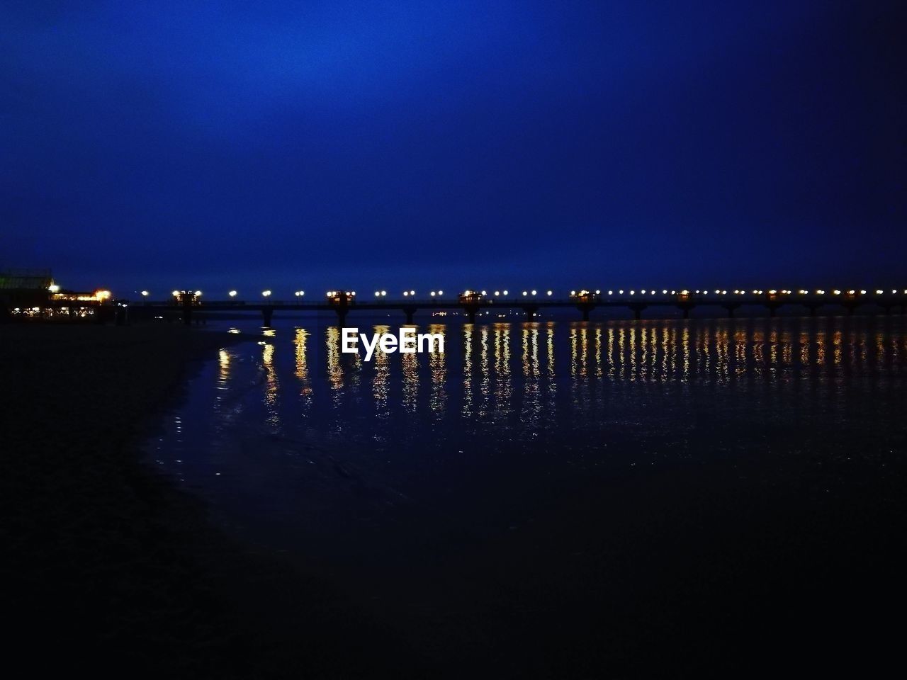 ILLUMINATED CITY BY SEA AGAINST CLEAR SKY