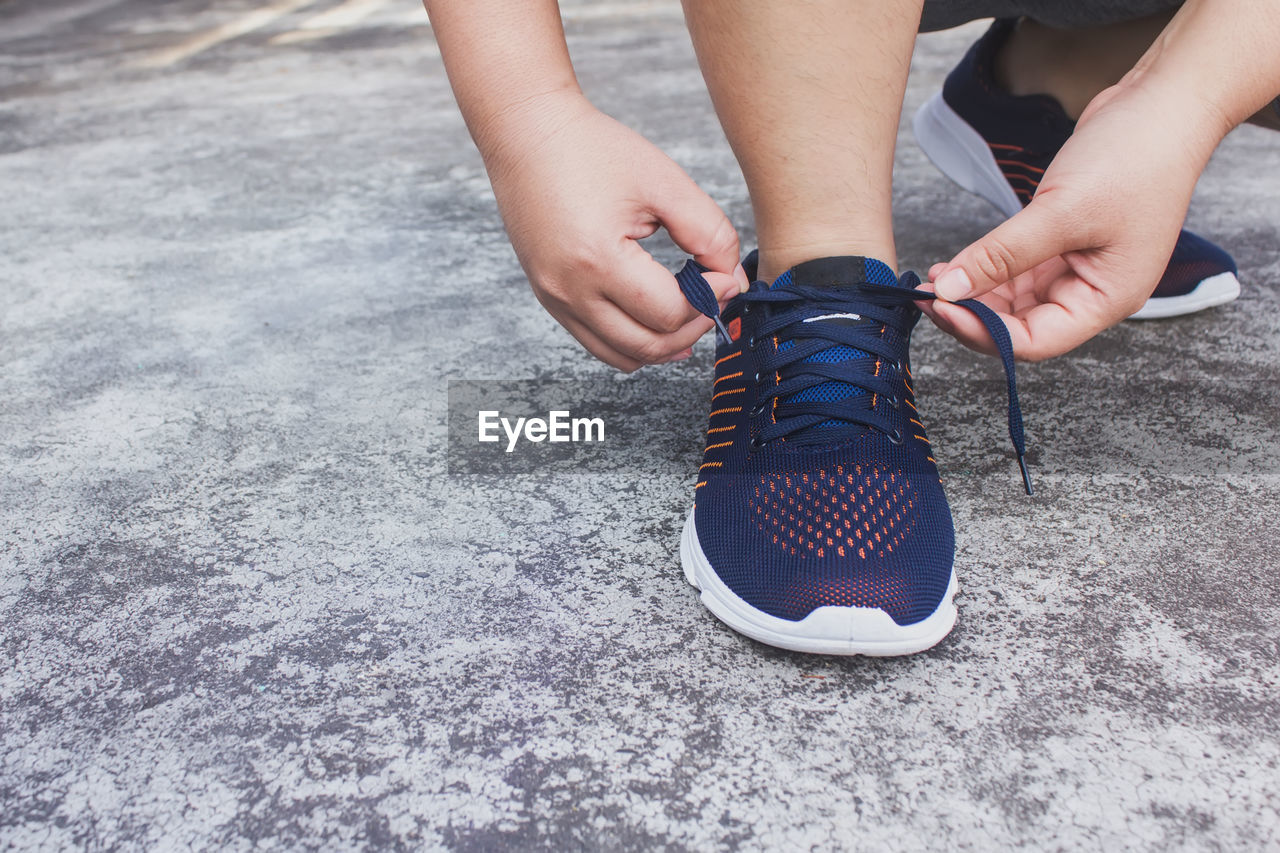 Low section of person tying shoelace on footpath