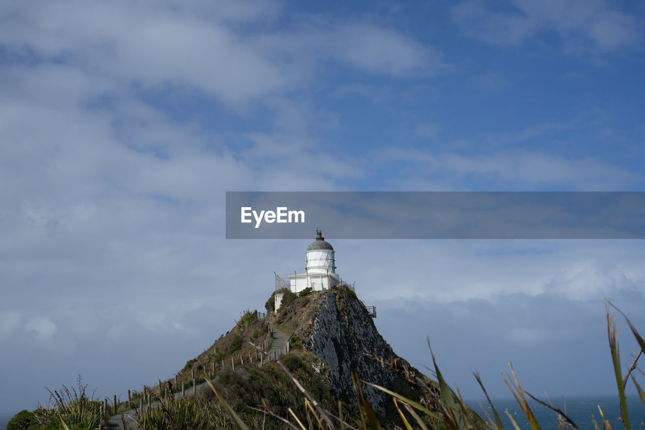 LOW ANGLE VIEW OF LIGHTHOUSE AMIDST BUILDINGS AGAINST SKY