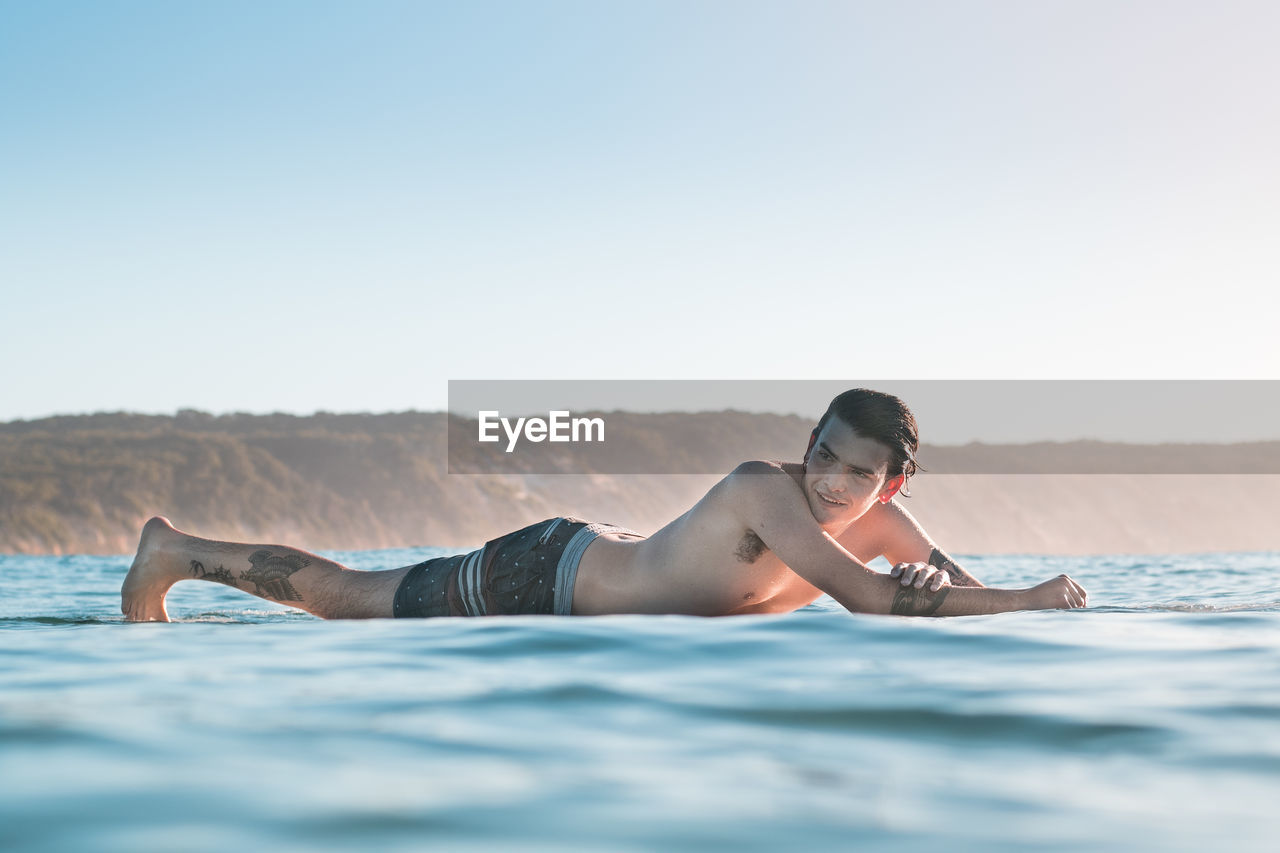 Young man relaxing at beach against clear sky