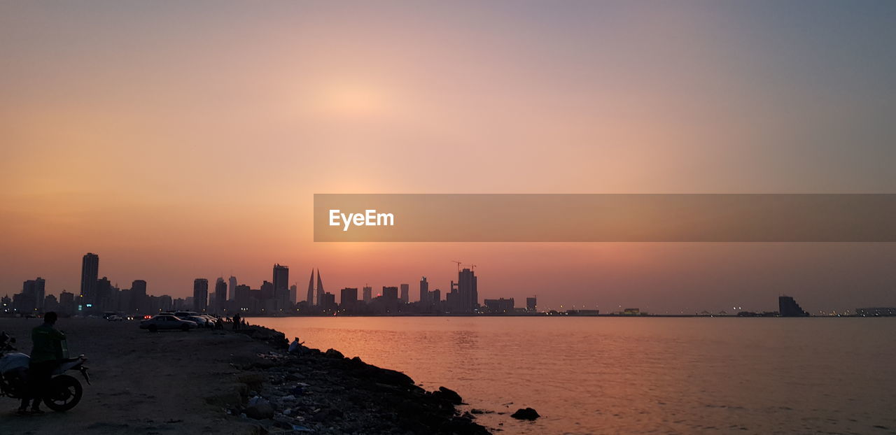 VIEW OF SEA AND BUILDINGS AGAINST SKY DURING SUNSET