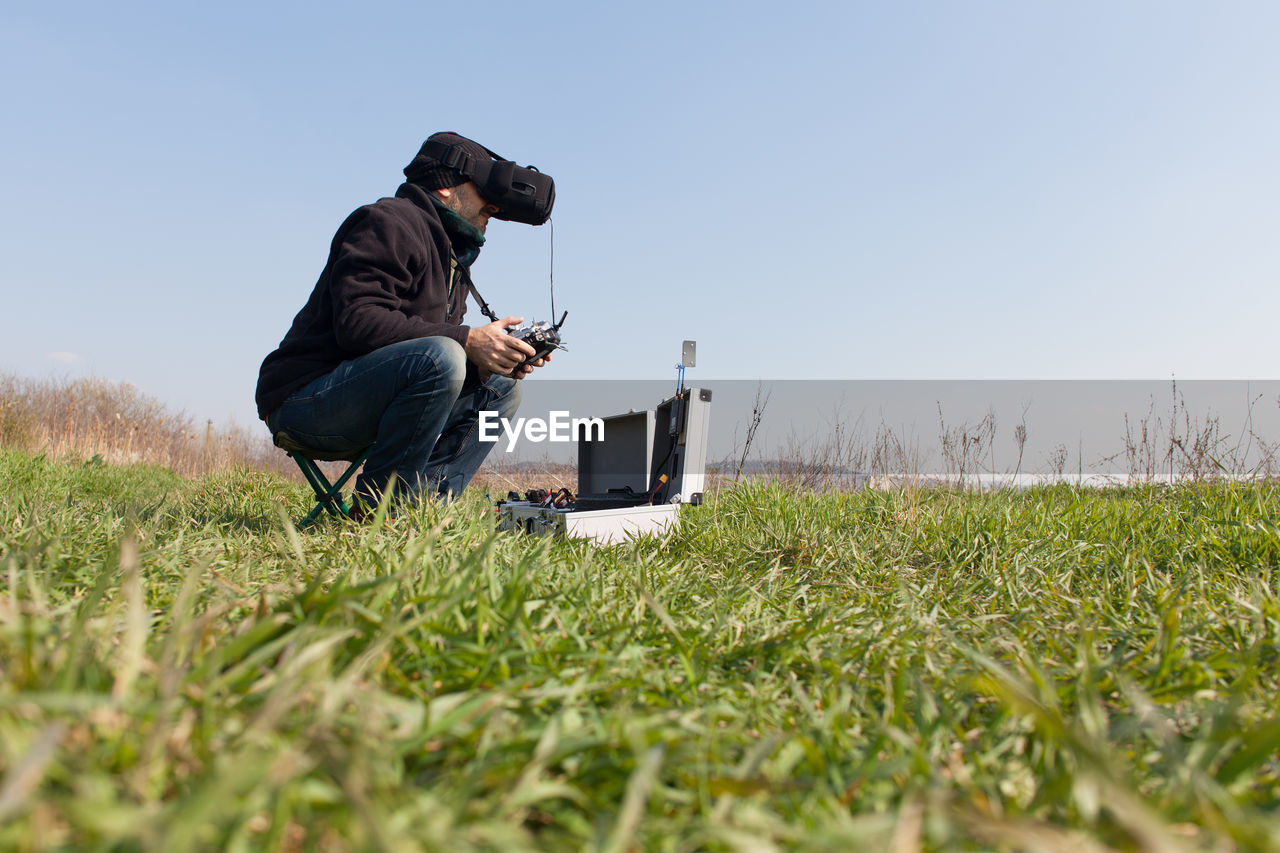 Man using virtual reality simulator while holding drone remote control on grassy field