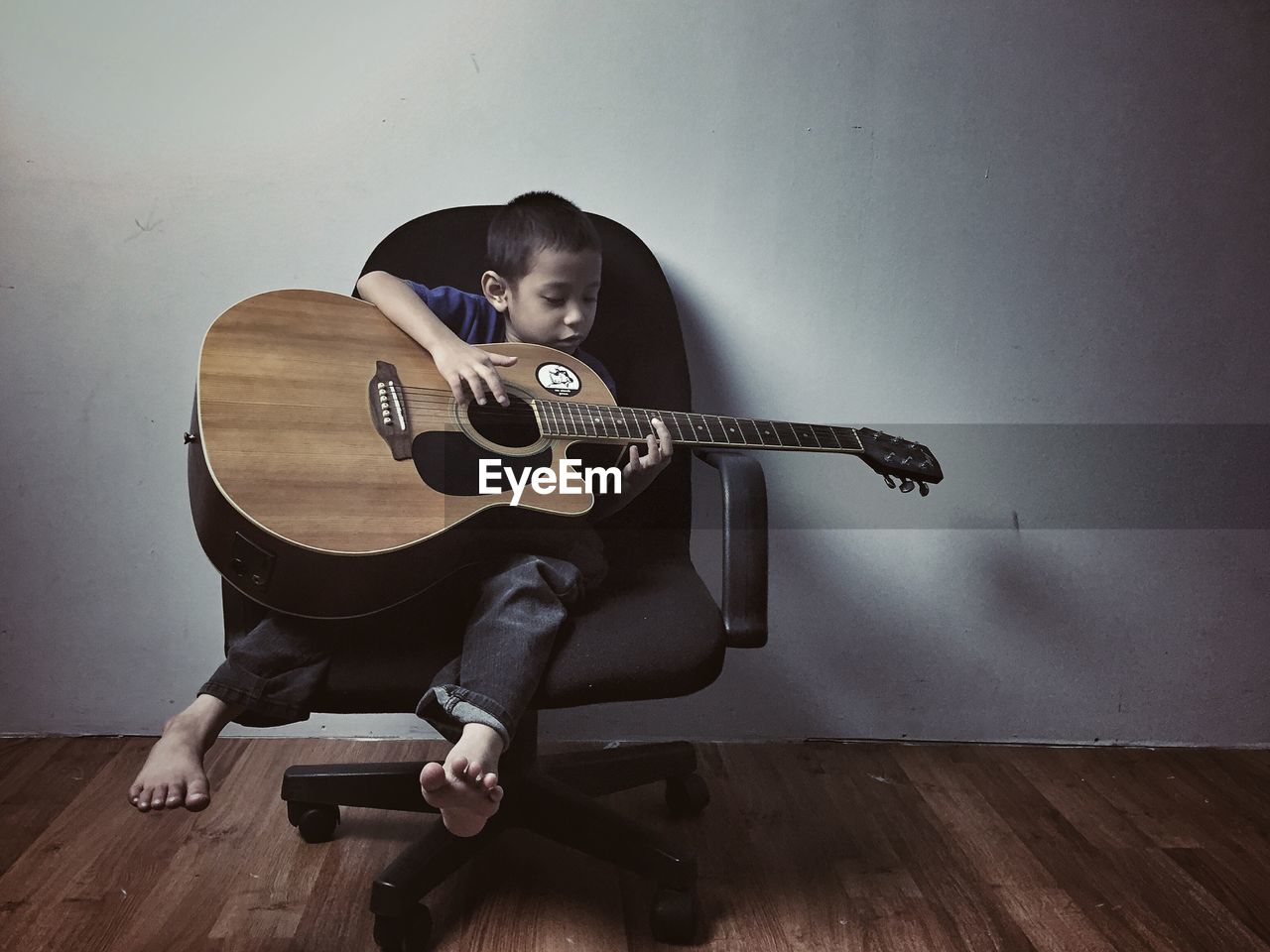 YOUNG WOMAN PLAYING GUITAR ON HARDWOOD FLOOR