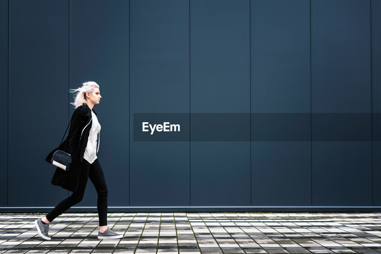 Side view of young woman walking on footpath against wall