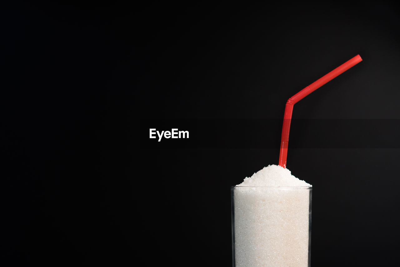 A glass of white sugar with straw against black background. concept of unhealthy eating and diabetis