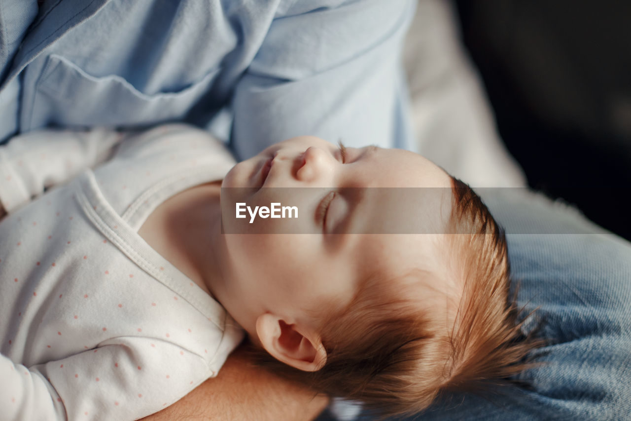 Midsection of father with sleeping baby girl on bed