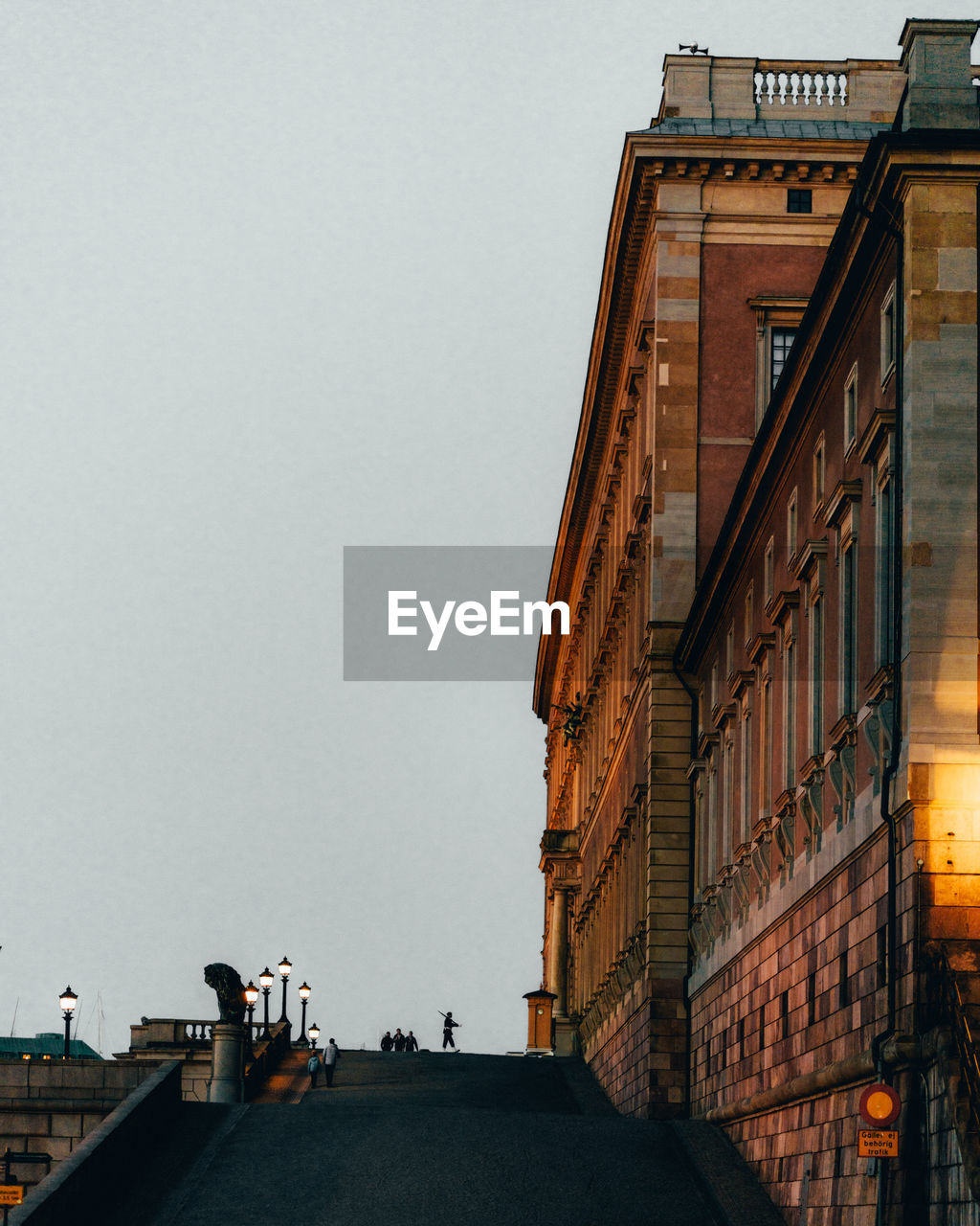 LOW ANGLE VIEW OF PEOPLE WALKING ON STREET AMIDST BUILDINGS AGAINST SKY