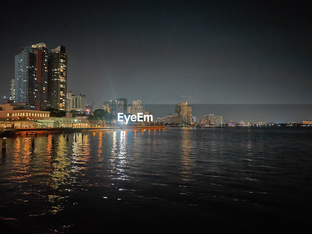 illuminated city by sea against sky at night