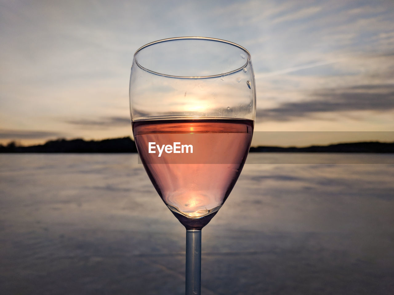 Glass of rose wine held up to sunset over frozen lake