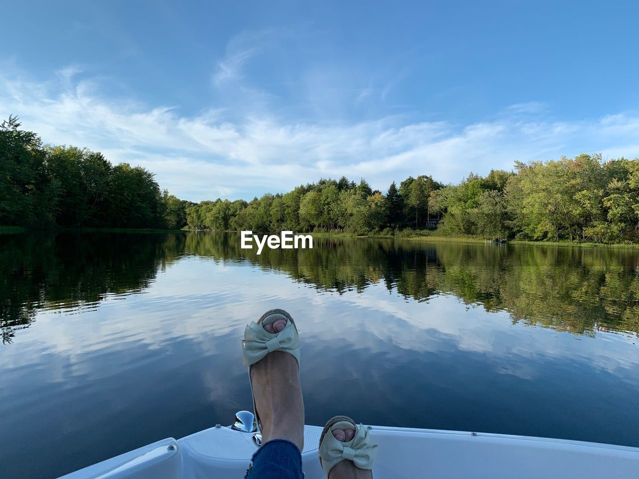 LOW SECTION OF PERSON IN LAKE BY TREES AGAINST SKY