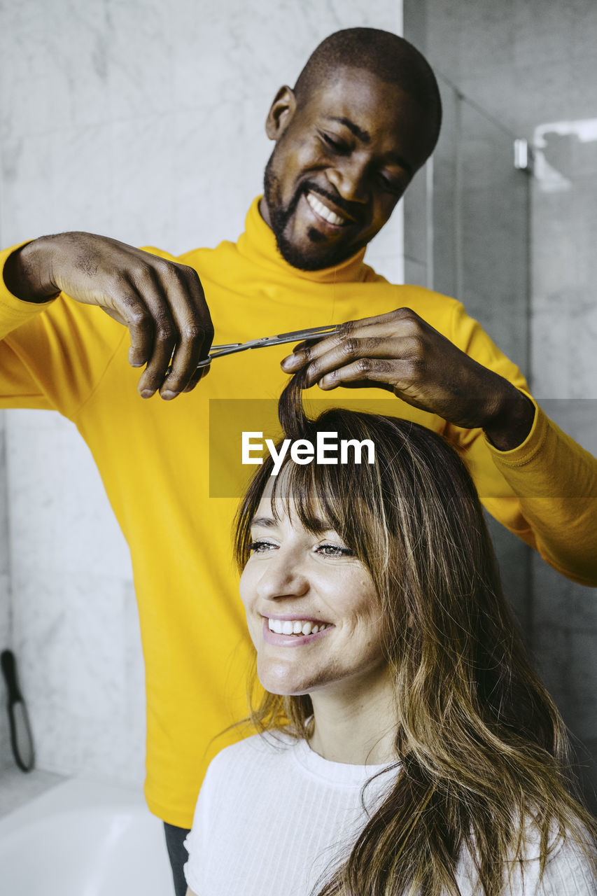 Smiling mid adult man cutting girlfriend hairs at home