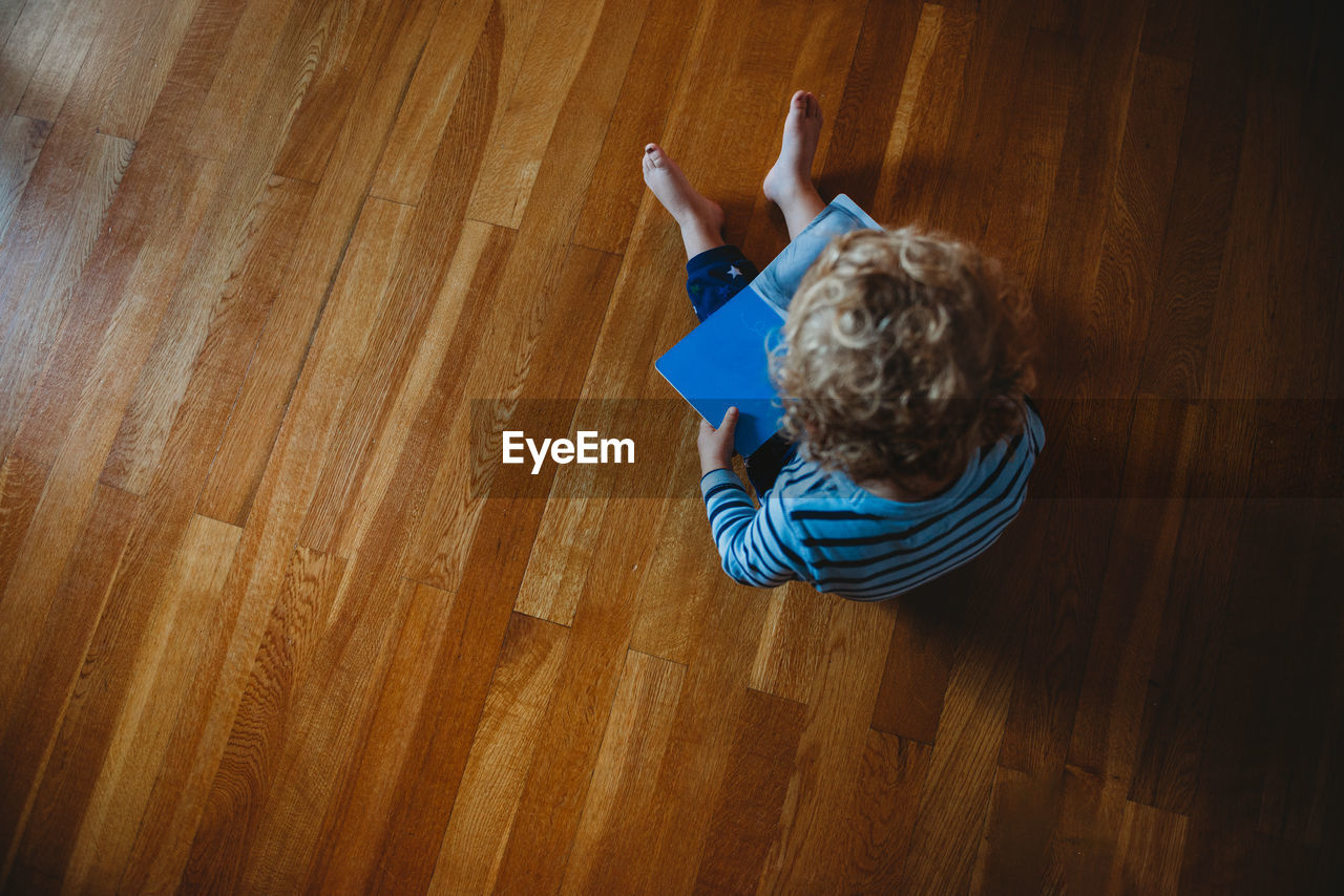 Top view of a young child with curls reading a book on the floor