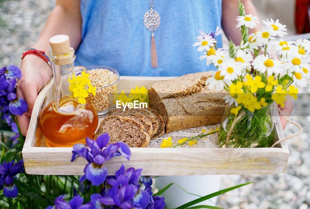 Close-up of young woman offering breakfast tray with flower bouquet