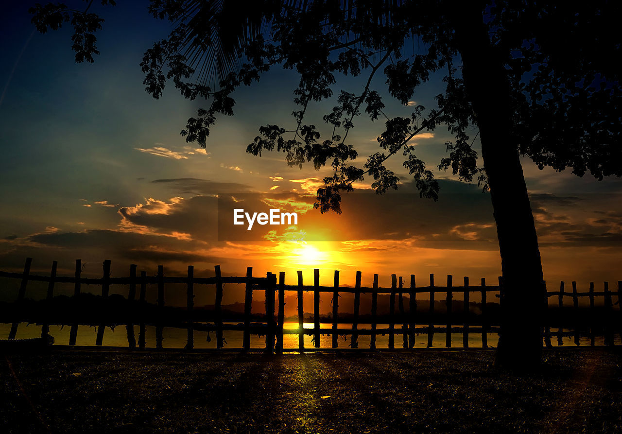 SILHOUETTE WOODEN POSTS IN SEA AGAINST ORANGE SKY