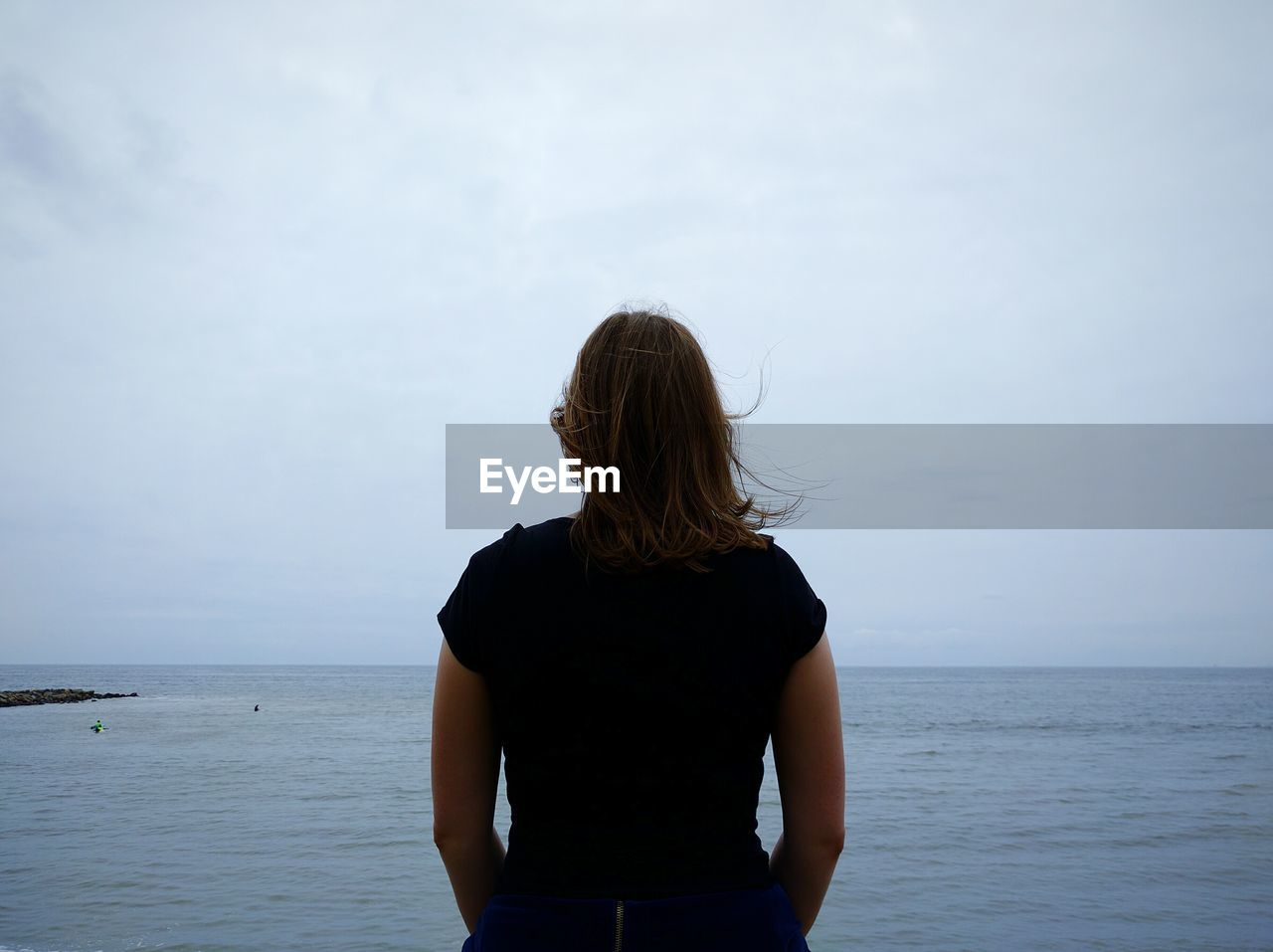 Rear view of woman standing in front of sea against sky