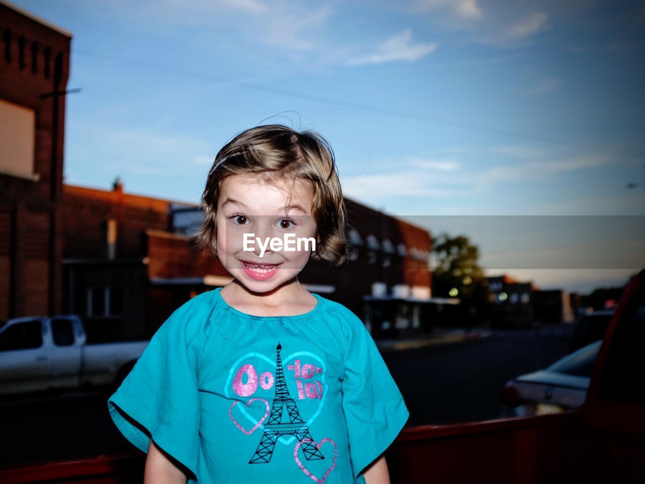 Portrait of girl in pick-up truck against buildings