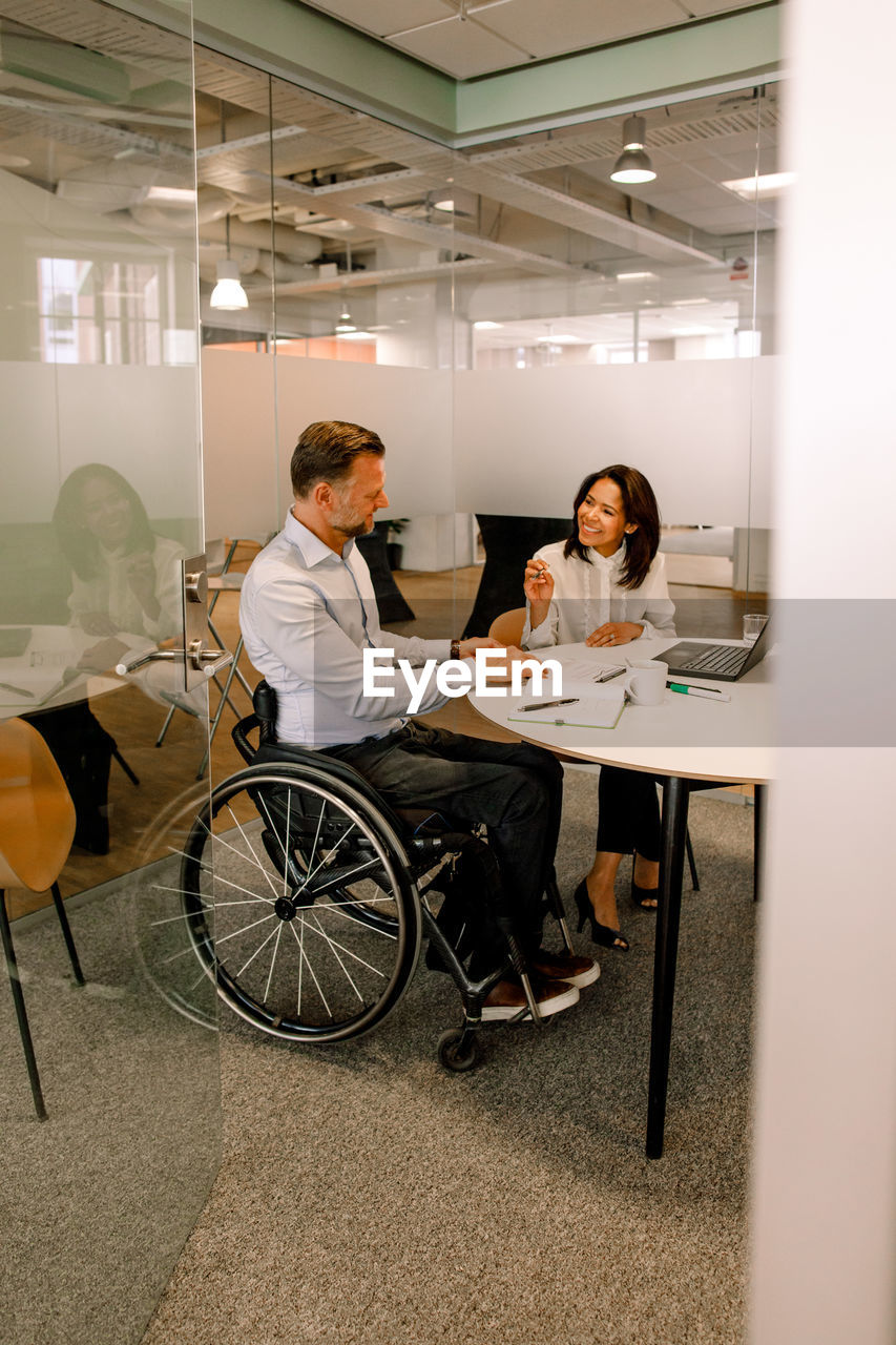 Smiling businesswoman discussing sales plans with disabled manager while sitting in board room