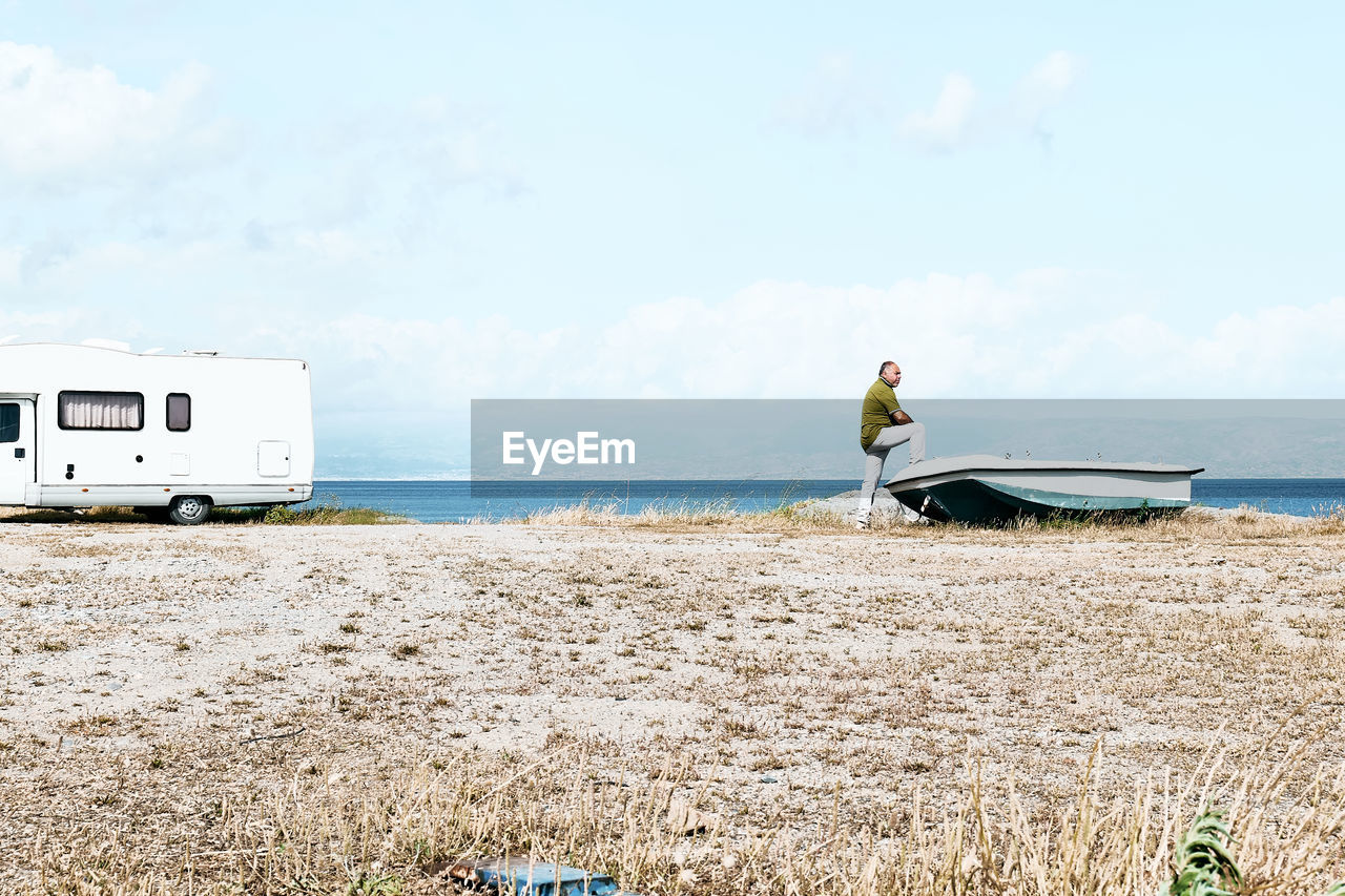 Man on the beach near the boat and white camper parked by the sea. sicily. ionian sea.