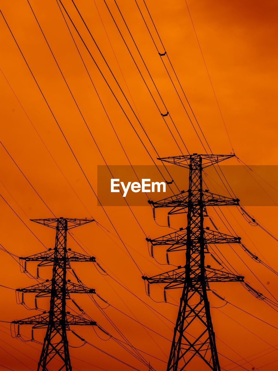 Low angle view of electricity pylons against sky during sunset