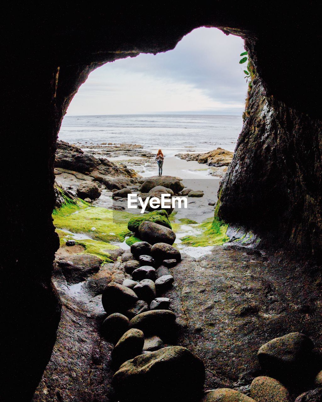 Woman standing on rock seen through arch of cave