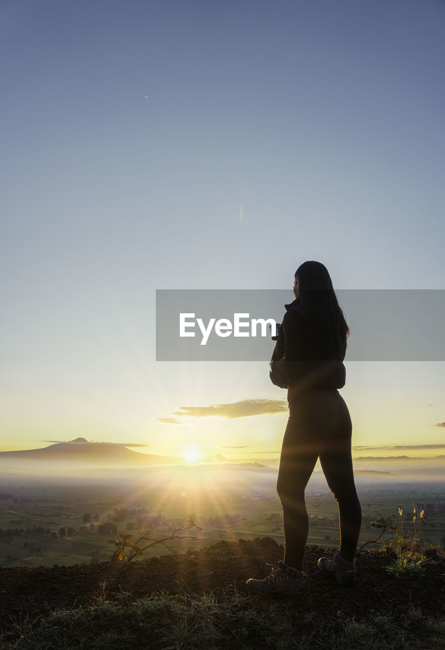 rear view of woman standing on beach against clear sky during sunset