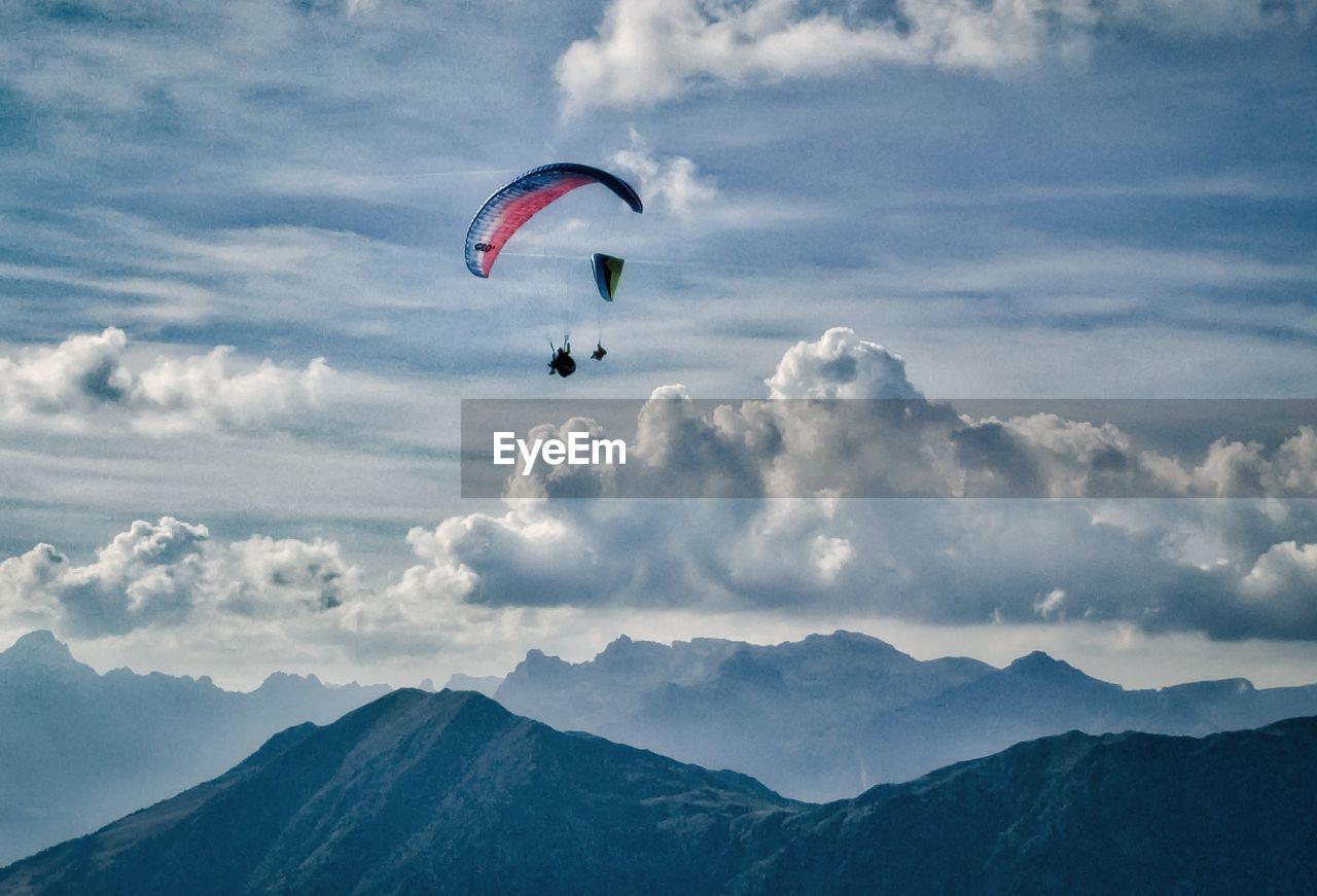 People paragliding above mountains against cloudy sky