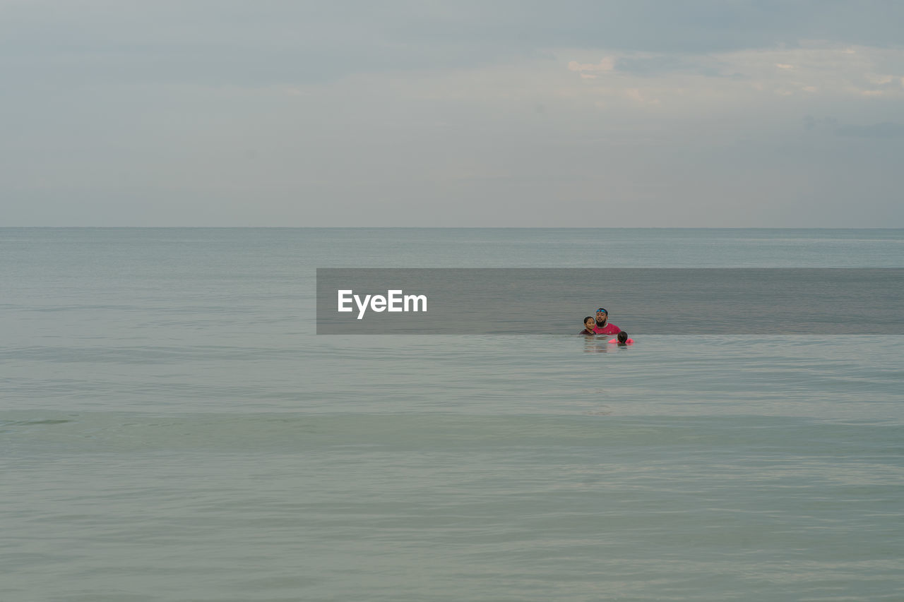 Father and daughter swimming in sea against sky