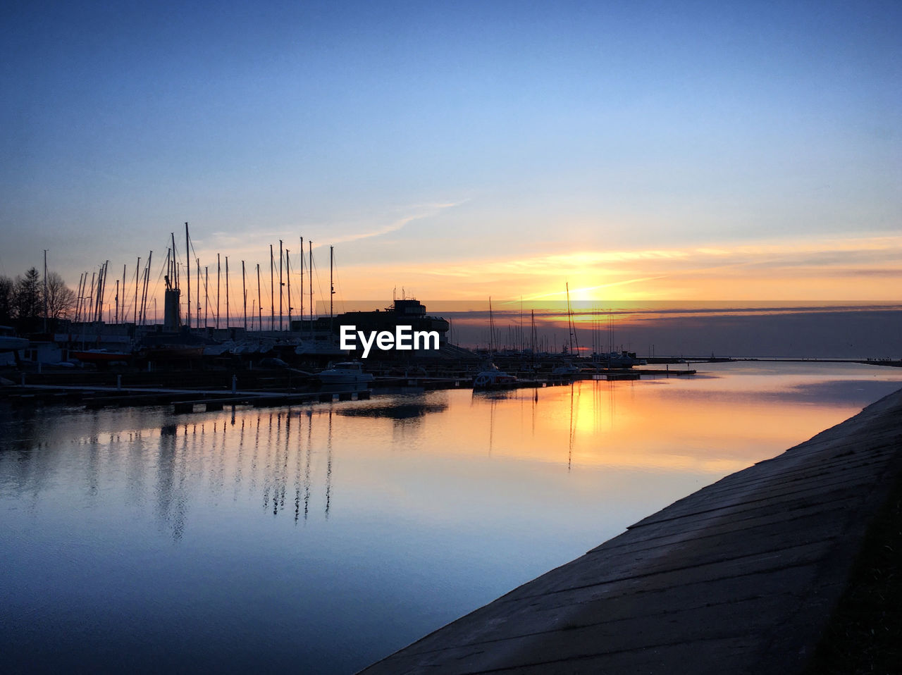 water, reflection, sky, sunrise, dawn, dock, sea, horizon, nautical vessel, morning, beauty in nature, nature, transportation, tranquility, scenics - nature, pier, tranquil scene, no people, architecture, harbor, mode of transportation, travel destinations, marina, ship, outdoors, travel, blue, sun, landscape, cloud, sailboat, idyllic, sunlight, twilight, beach, environment, vehicle, ocean, land, bay, boat, city, built structure