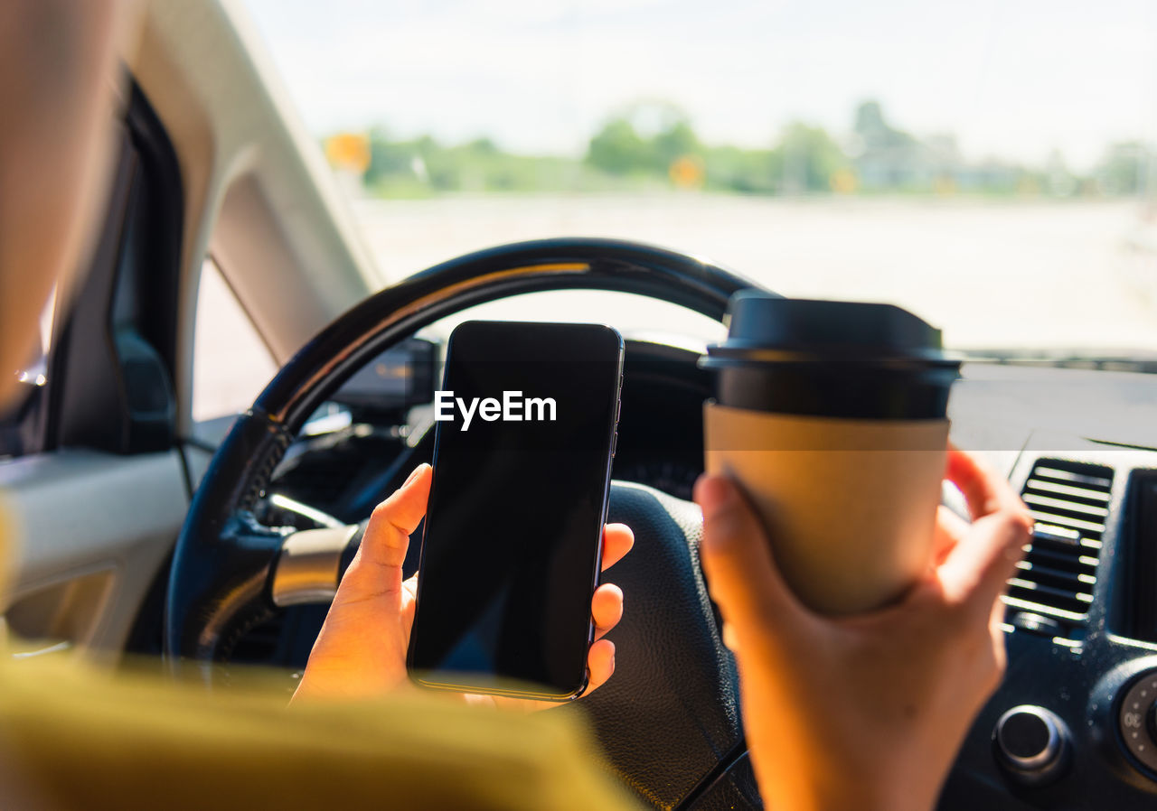 Cropped hands of woman holding smart phone and coffee in car