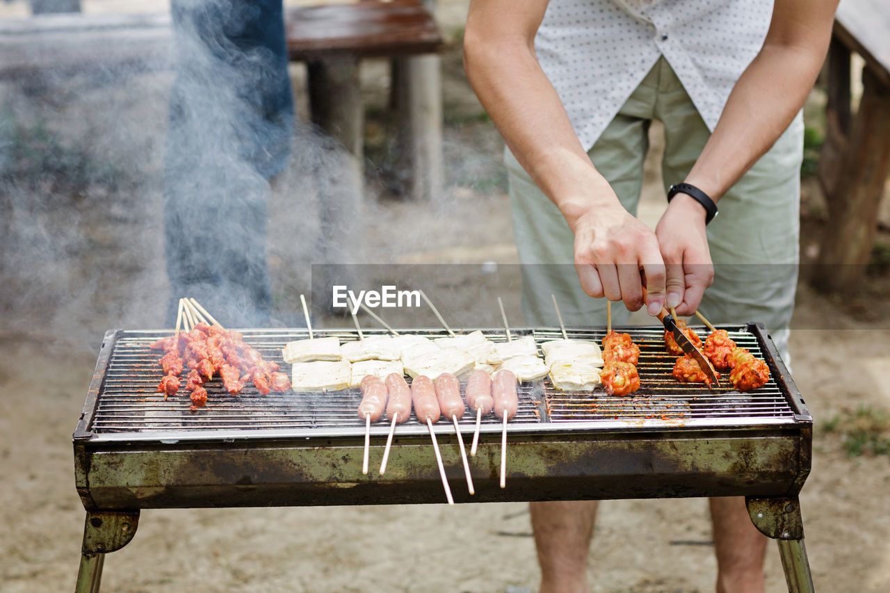 midsection of man preparing meat on barbecue grill