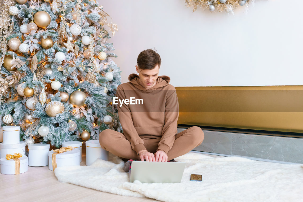 A man sitting on floor near christmas tree orders online goods on black friday