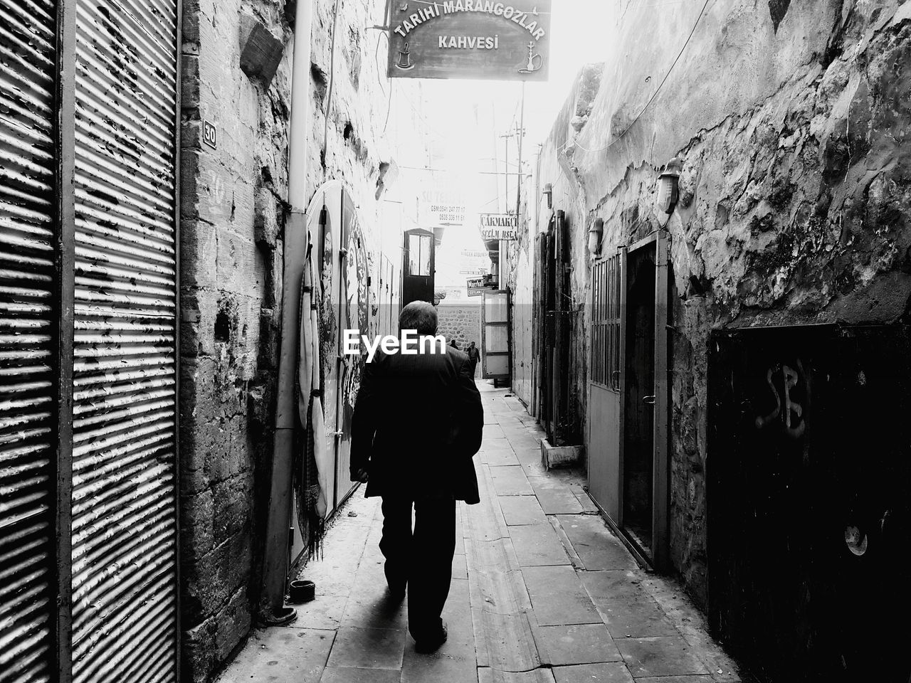 FULL LENGTH REAR VIEW OF MAN WALKING ON FOOTPATH AMIDST BUILDINGS