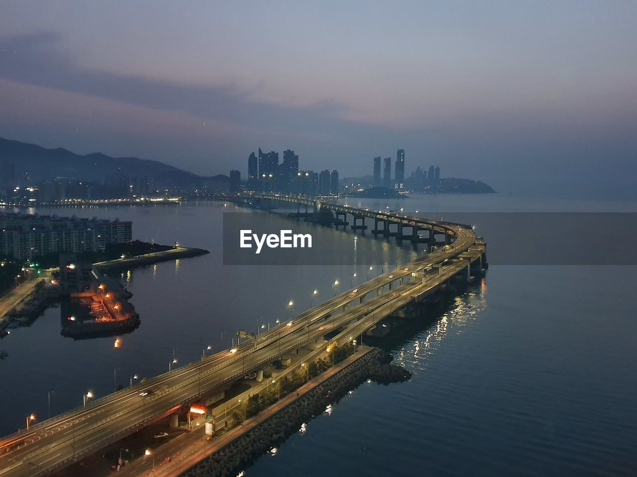 High angle view of illuminated city by river against sky